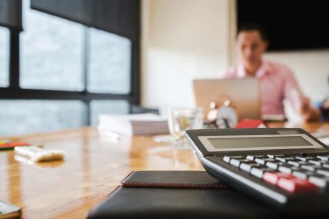 A person works on a laptop with a calculator